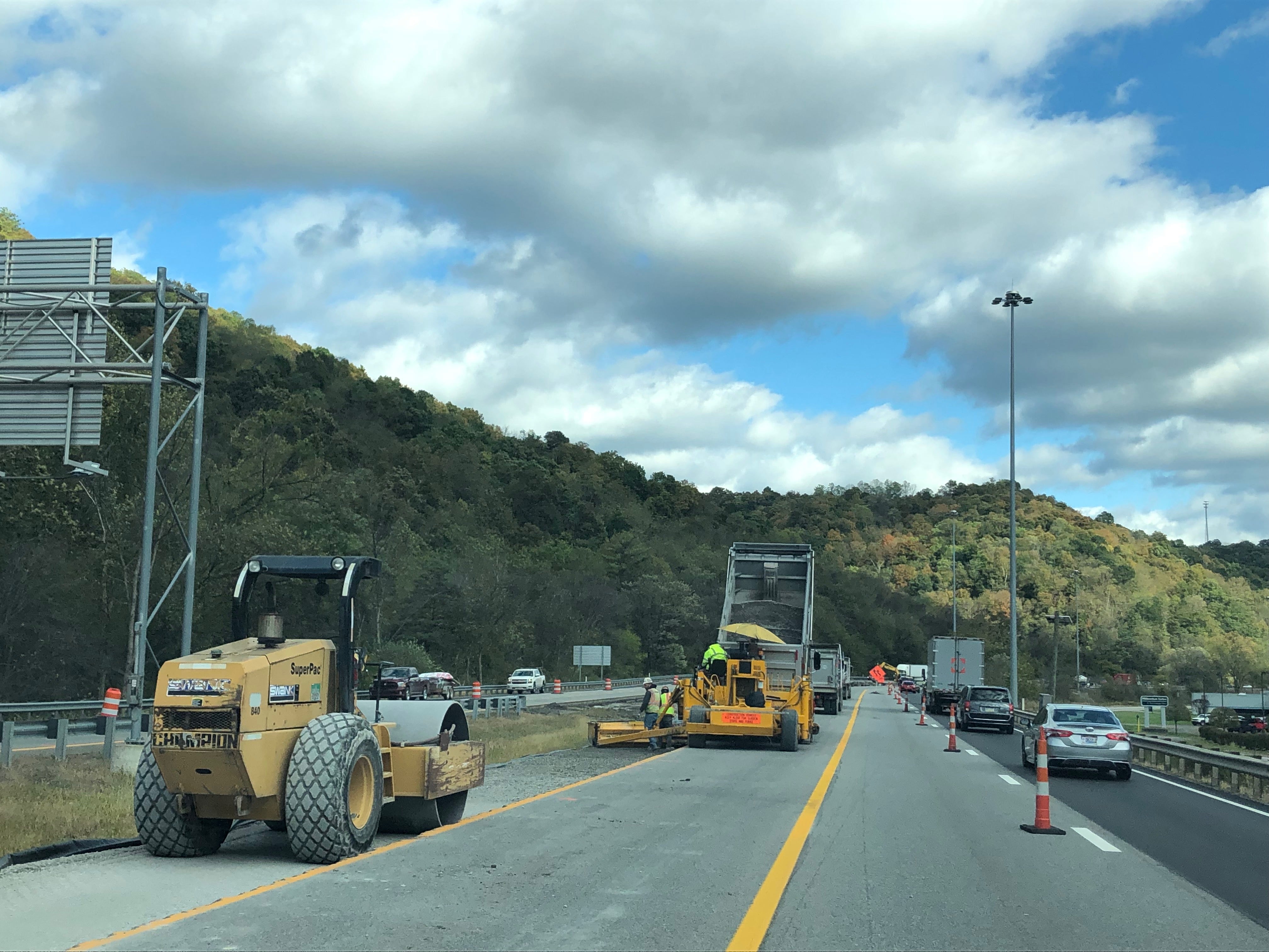 A yellow road roller and paving machinery operating on the I-70 construction site in Wheeling under a cloudy sky.