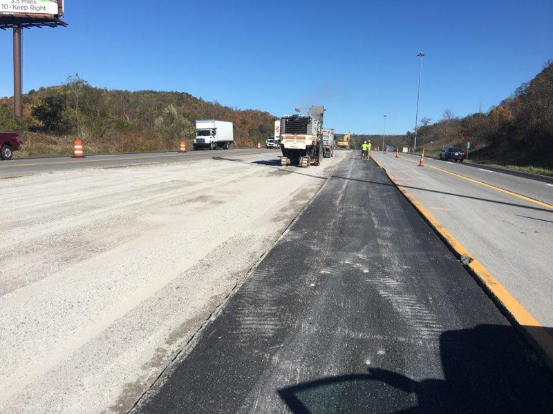A large milling machine removing the top layer of asphalt on the I-70 corridor in Wheeling, revealing a grey milled pavement surface under a clear blue sky.