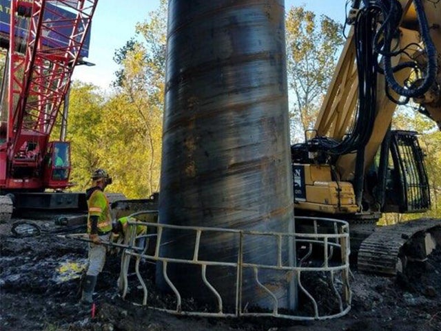Construction crew and heavy equipment installing a large metal foundation casing for a bridge pier on the I-70 Forward project.