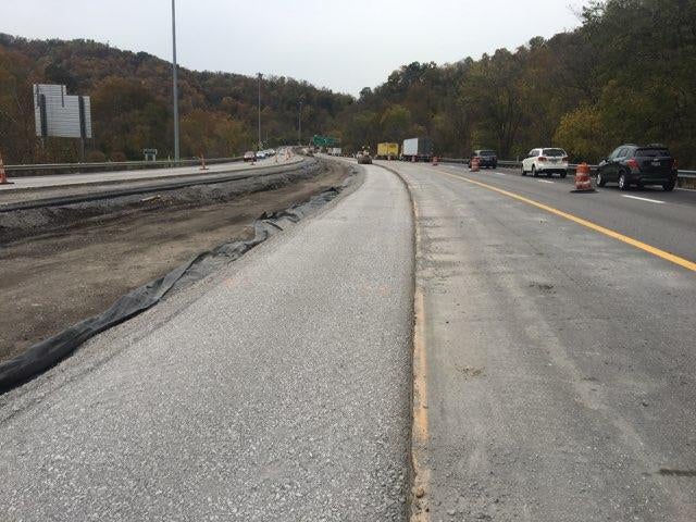 View of milled pavement and shoulder rehabilitation work on the I-70 corridor in Wheeling, with active traffic moving in the adjacent lane.