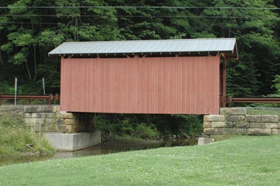 Side view of the red wooden Fish Creek Covered Bridge spanning a small creek on stone abutments