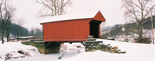 Red Walkersville Covered Bridge spanning a partially frozen creek in a snowy winter landscape
