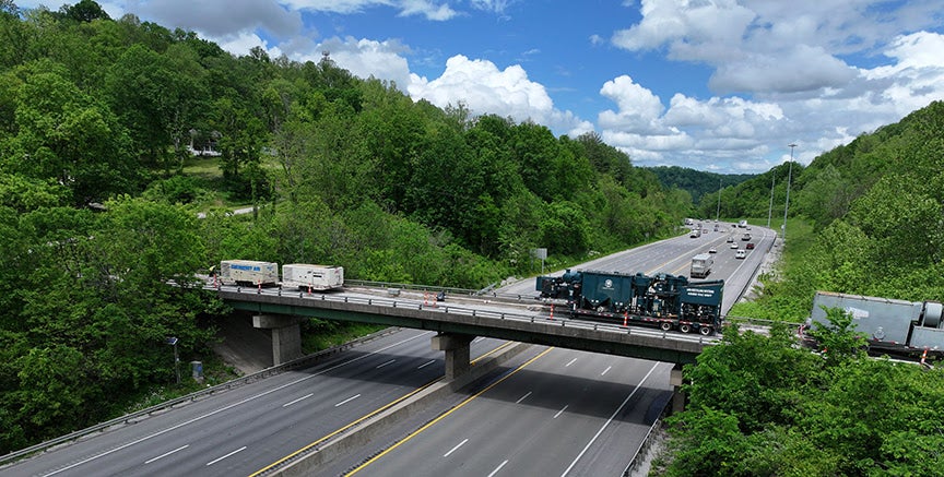 Overpass bridge with heavy machinery crossing a multi-lane highway surrounded by green hills.