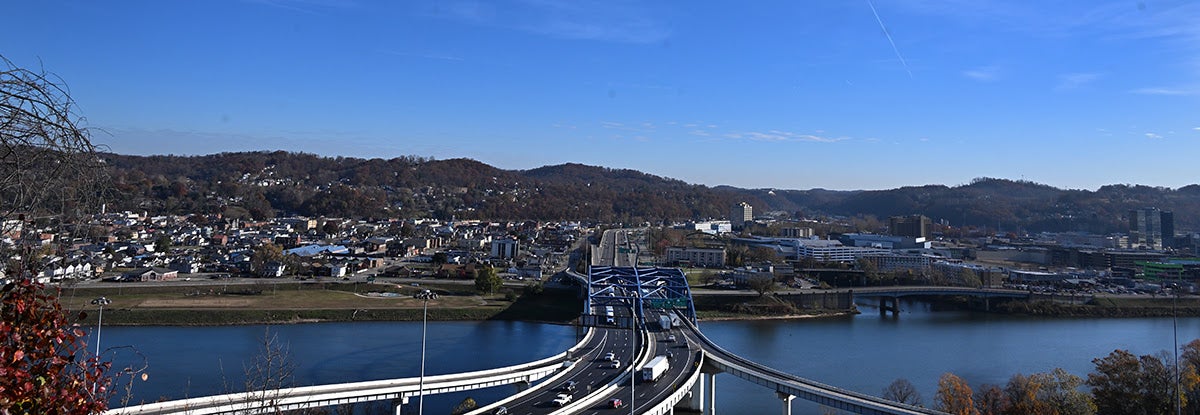 A wide panoramic view captures vehicles traveling across the newly completed road surface of the Fort Hill Bridge under a clear blue sky.