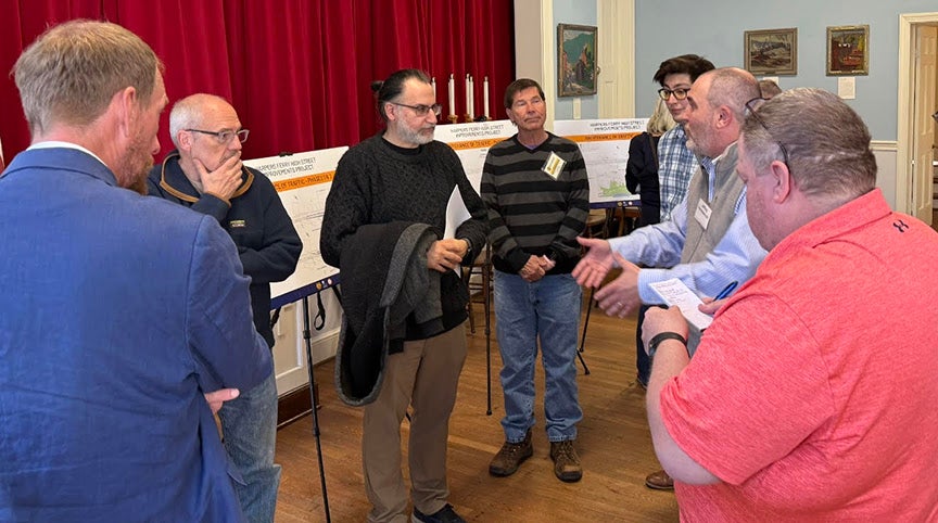 A group of residents and project officials engaged in discussion in front of presentation boards at the Harpers Ferry High Street improvements public meeting.