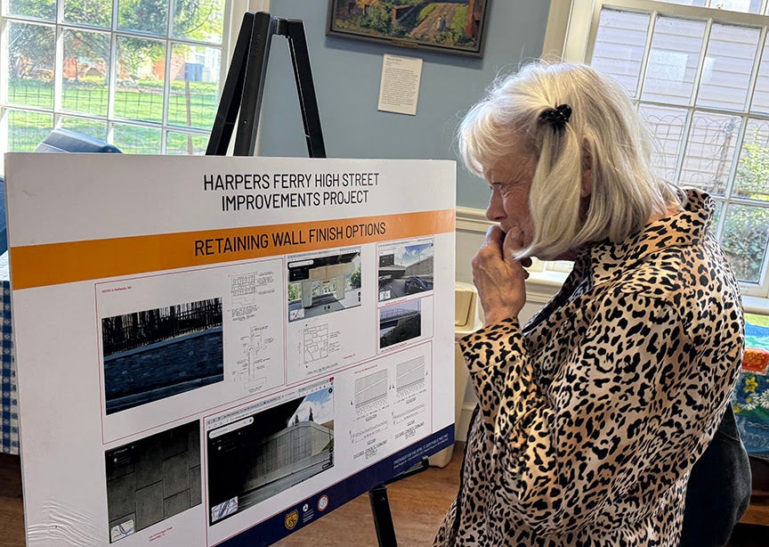 A resident closely examining a display board showing retaining wall finish options at the Harpers Ferry High Street improvements public meeting.