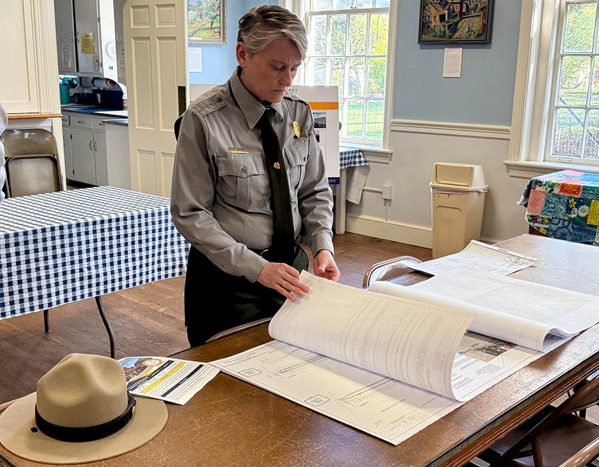 A National Park Service ranger reviewing large printed project plans at a table during the Harpers Ferry public meeting.