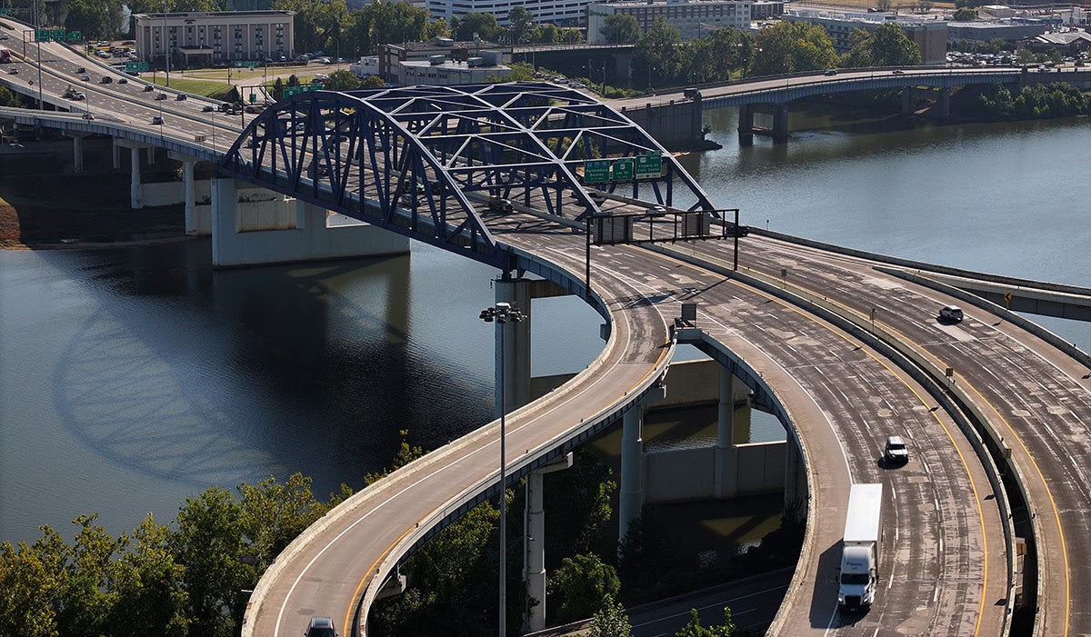 High-angle view of a blue steel arch bridge over a river with connecting highway ramps and traffic.