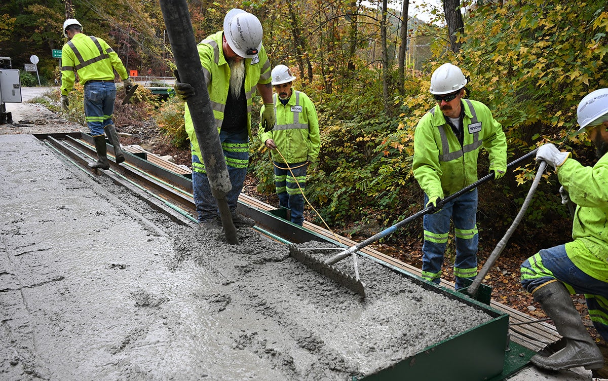 A construction crew working to pour, spread, and smooth fresh concrete on a newly reconstructed bridge deck surface.