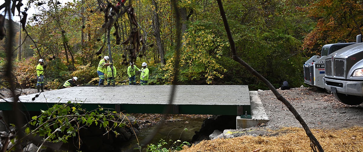 A concrete pump truck boom pouring fresh concrete onto a bridge deck while construction workers manage the flow and distribution.