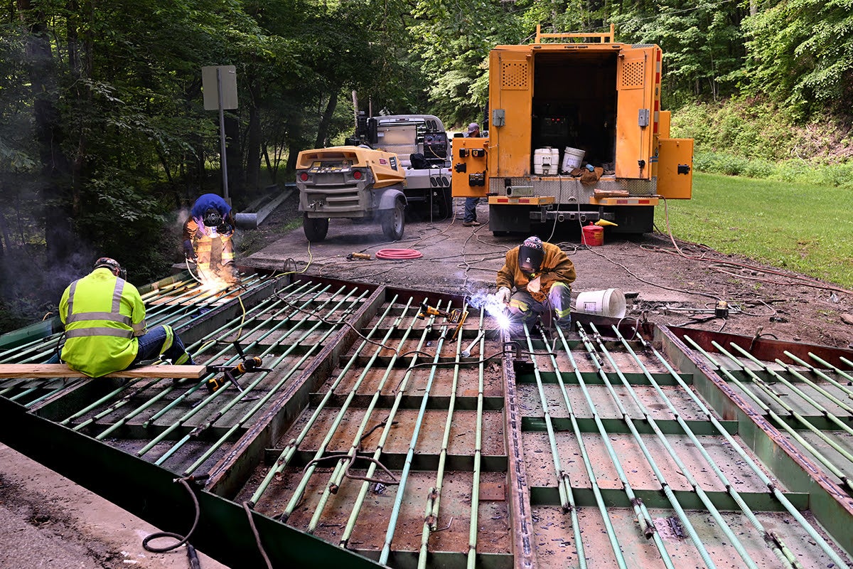 Construction workers use welding torches to secure the metal grid framework of a new bridge deck in Kanawha State Forest.